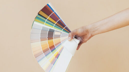 Close up photo of female hand holding a presentation color palette with color samples over a nude background.