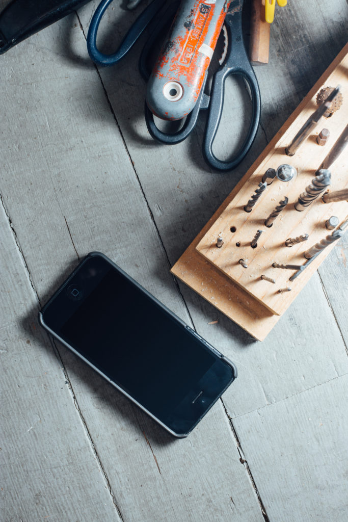 tools, drill bits, and a smartphone on a wood surface