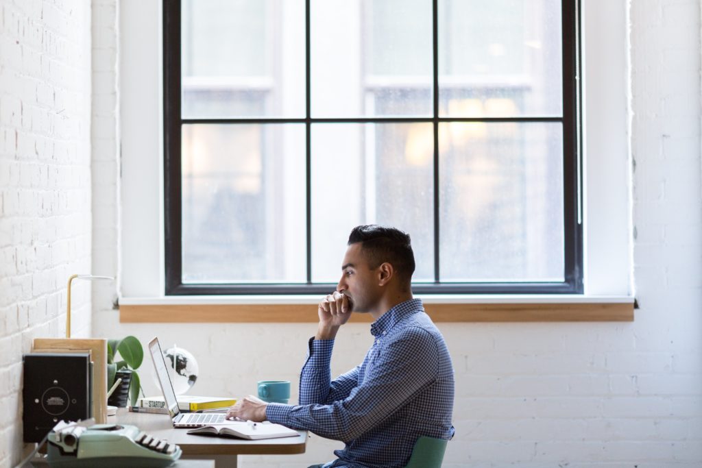 man thinking at a desk by a big window