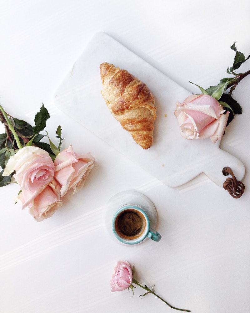 croissant and espresso on a white marble platter with pink roses