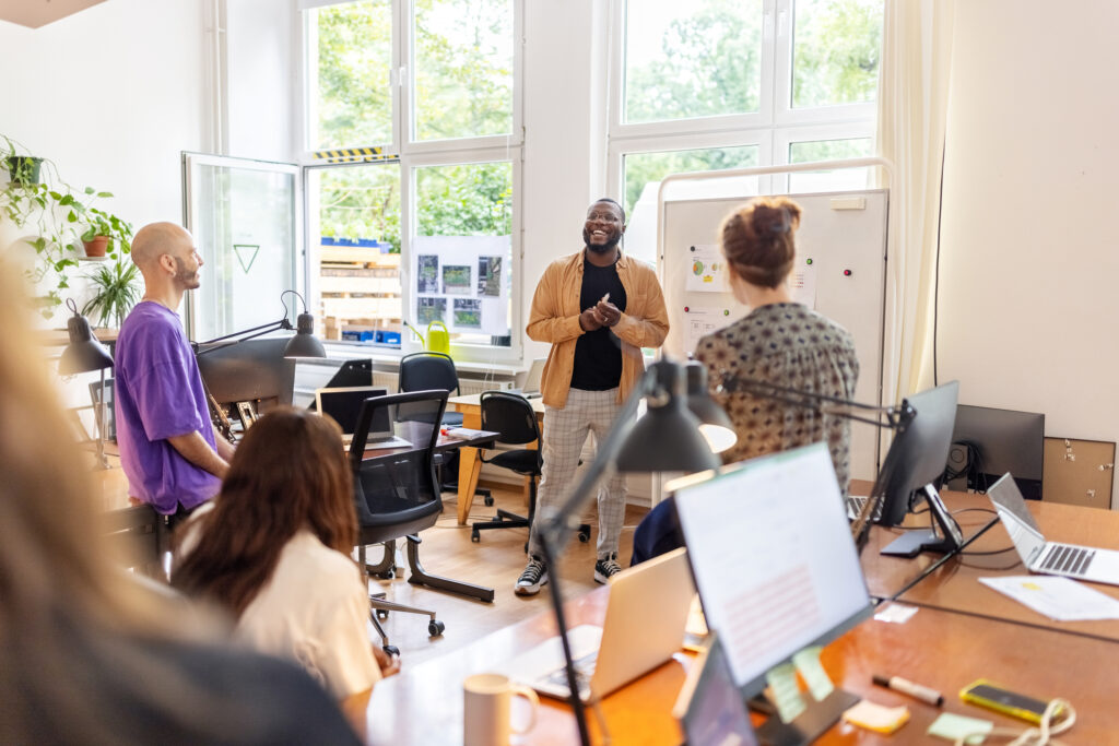 African man standing by whiteboard and giving presentation to startup team at office. Man explaining marketing strategy using statistical graphs to colleagues at office.