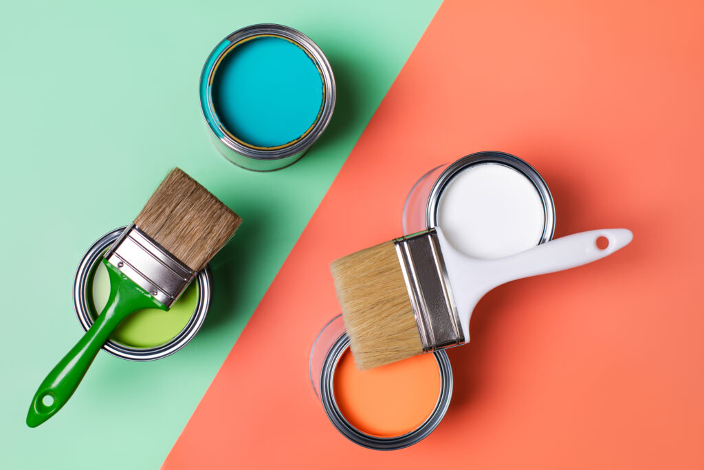 Composition of various paints in cans and paintbrushes placed on green and orange background 