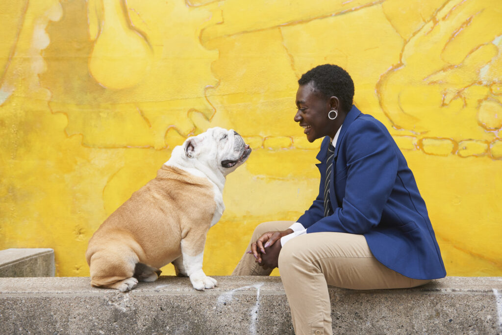 Androgynous Black woman sitting with dog near mural