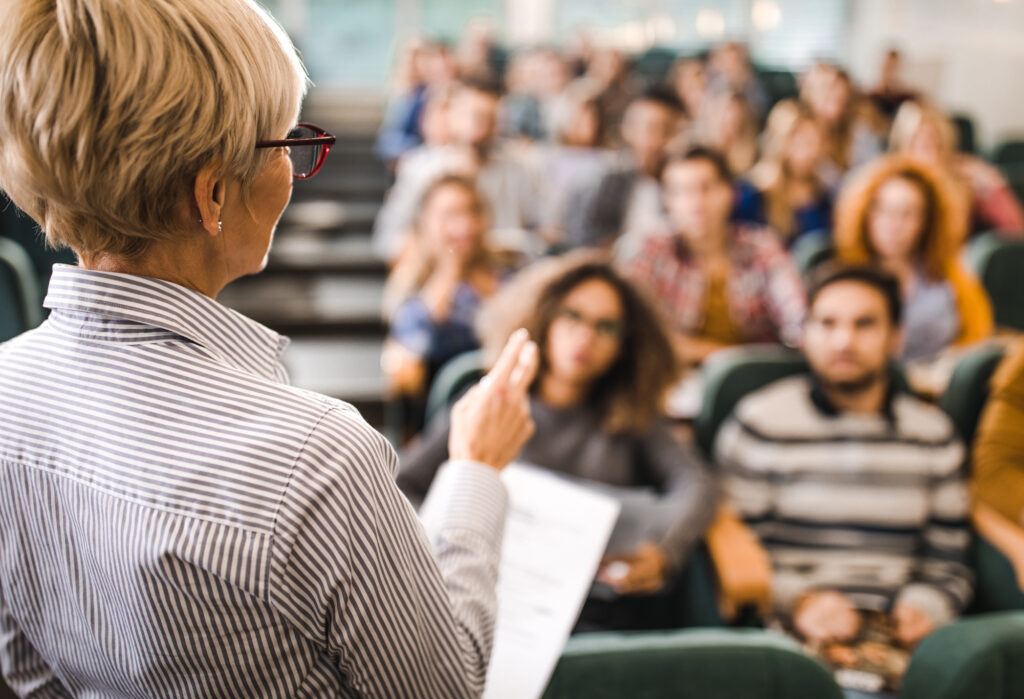 Back view of a senior professor talking on a class to large group of students.