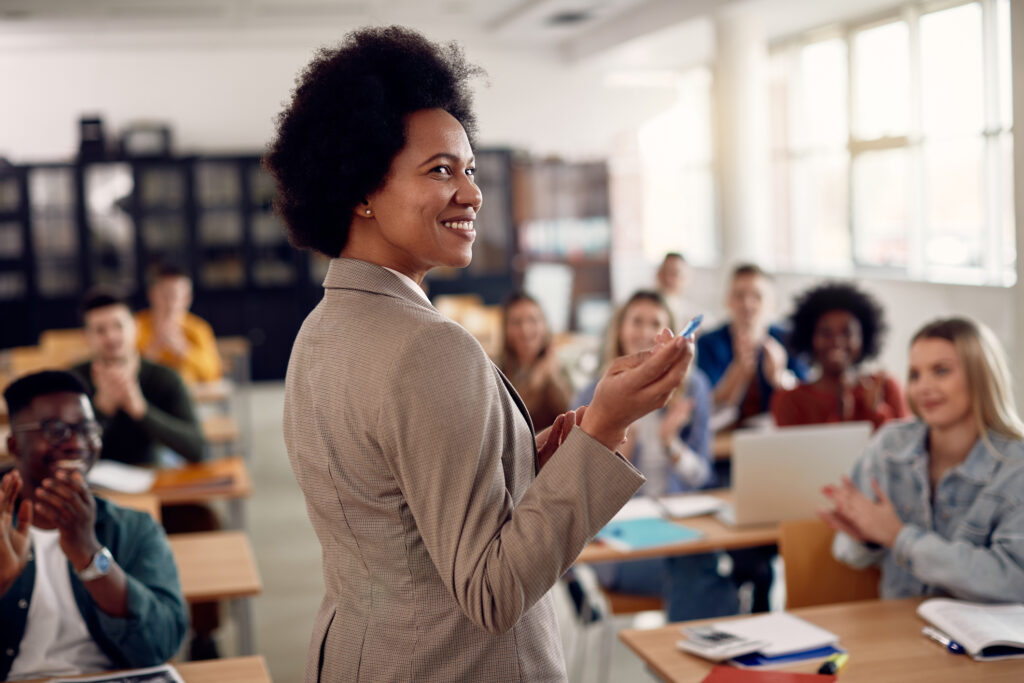 Happy African American professor receives applause from her students while lecturing them in the classroom.