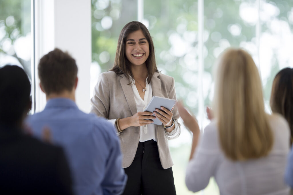 A women in front of an audience presenting a sales deck.