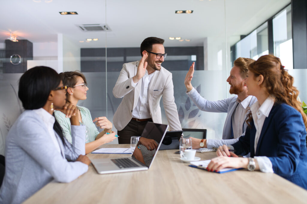 Two businessmen are congratulating one another with high five after successful sales team meeting and a good presentation given by the manager in the conference room.