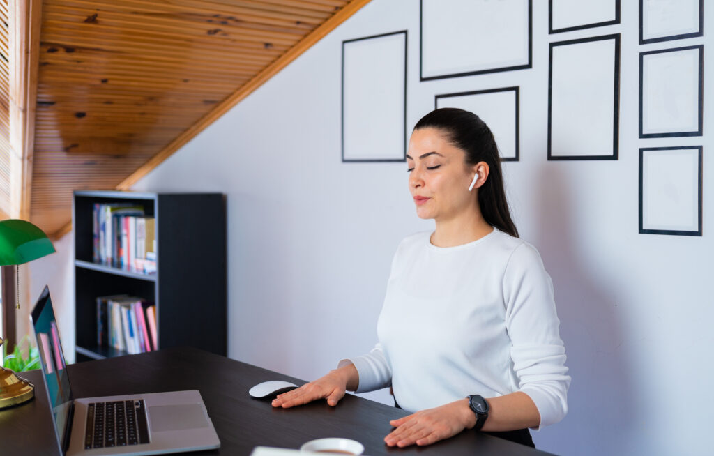 Relaxed calm business woman take deep breath of fresh air resting with eyes closed at work in home office. Doing office yoga and meditating with closed eyes.