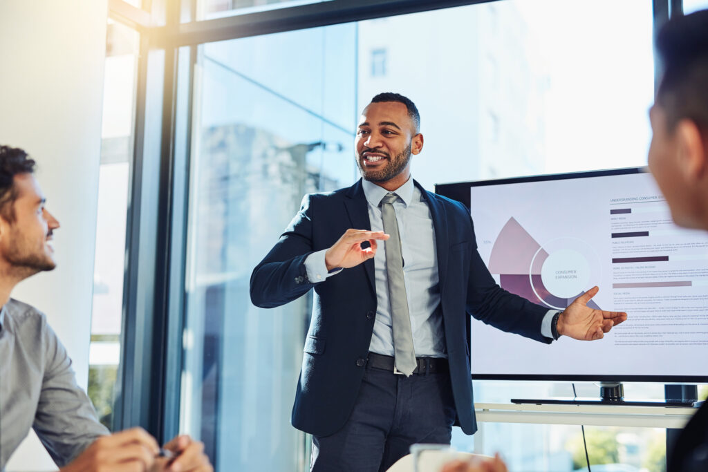 Shot of a young businessman delivering a presentation to his colleagues in the boardroom of a modern office. Useinf effective presentation skills and confident body language.