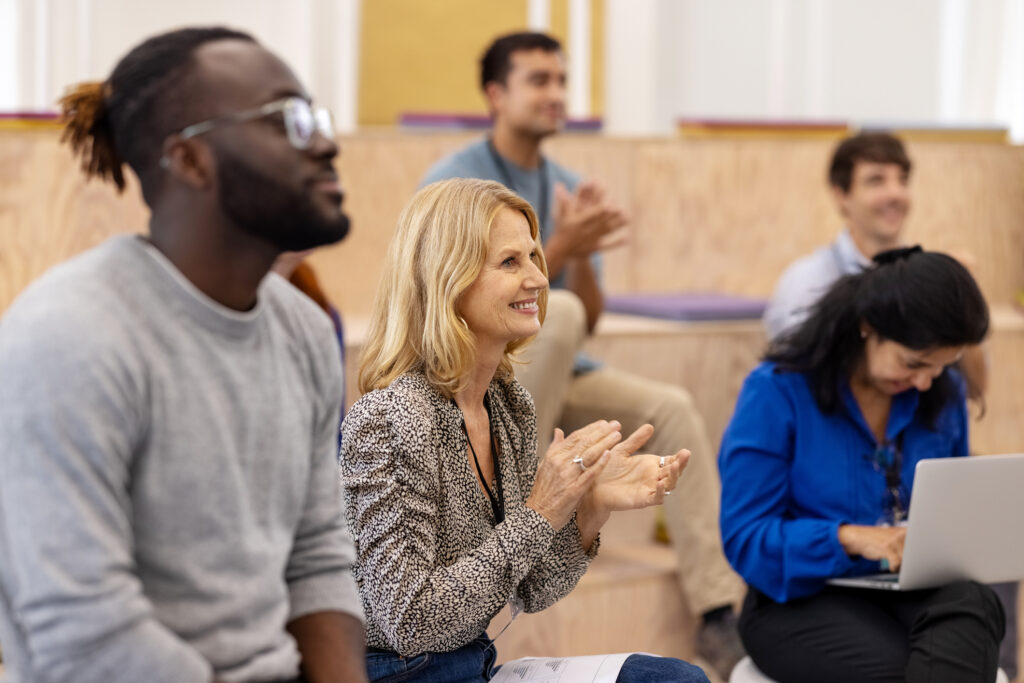 Group of multiracial men and women applauding in a seminar. Multi-ethnic group sitting in the audience clapping hands after a conference.