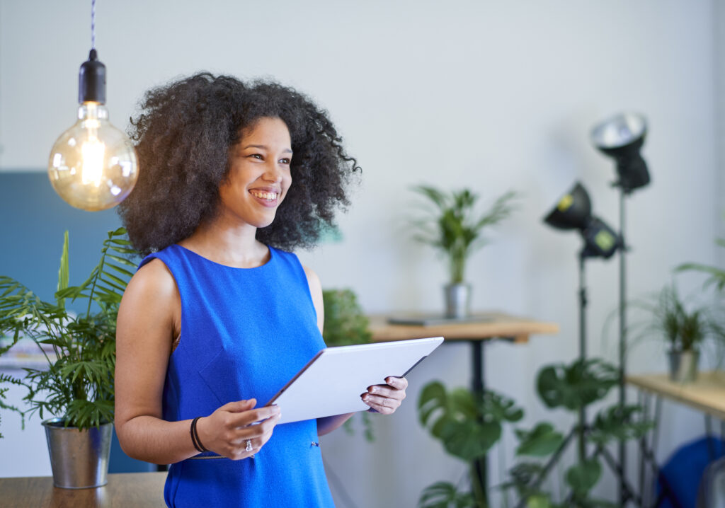 Young female at work, holding tablet computer and smiling in modern sustainable office space with tablet computer.