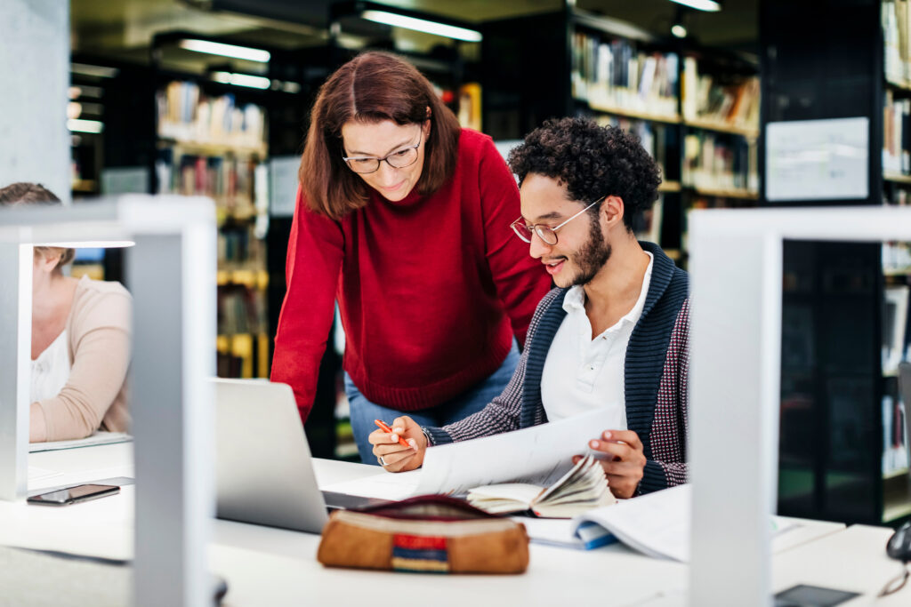 A Teacher helping a young student with his studies while working in a public library.