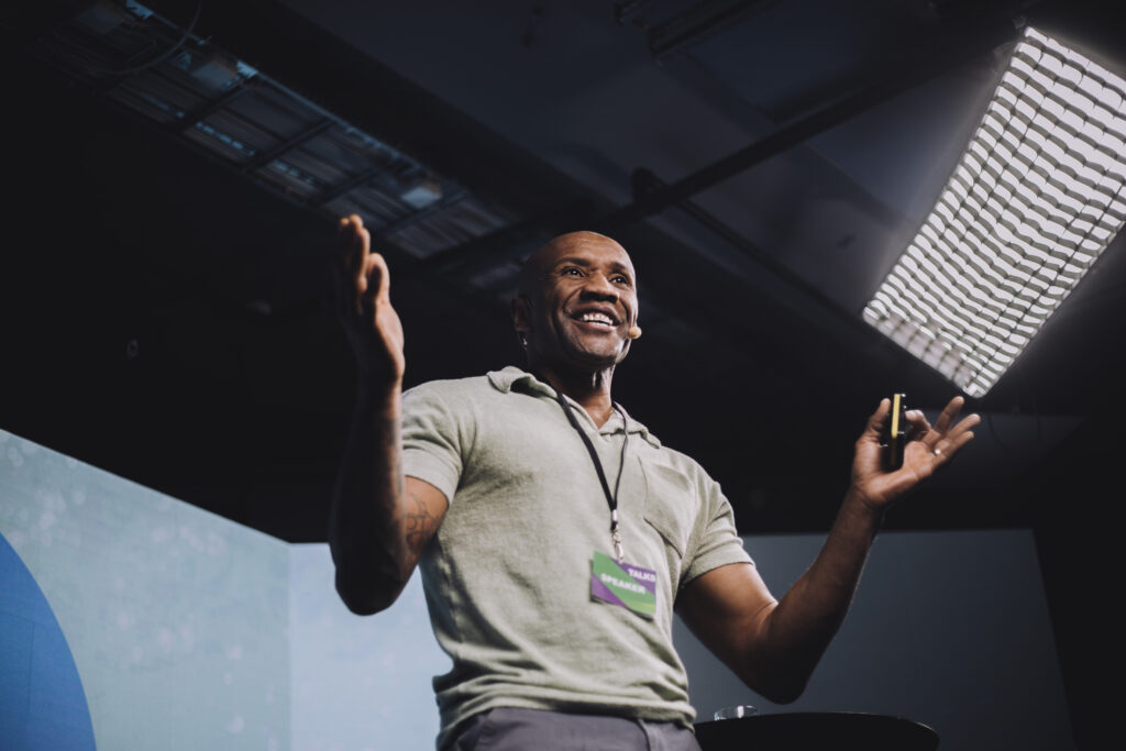 A man presenting on stage, giving a Ted Talk presentation.