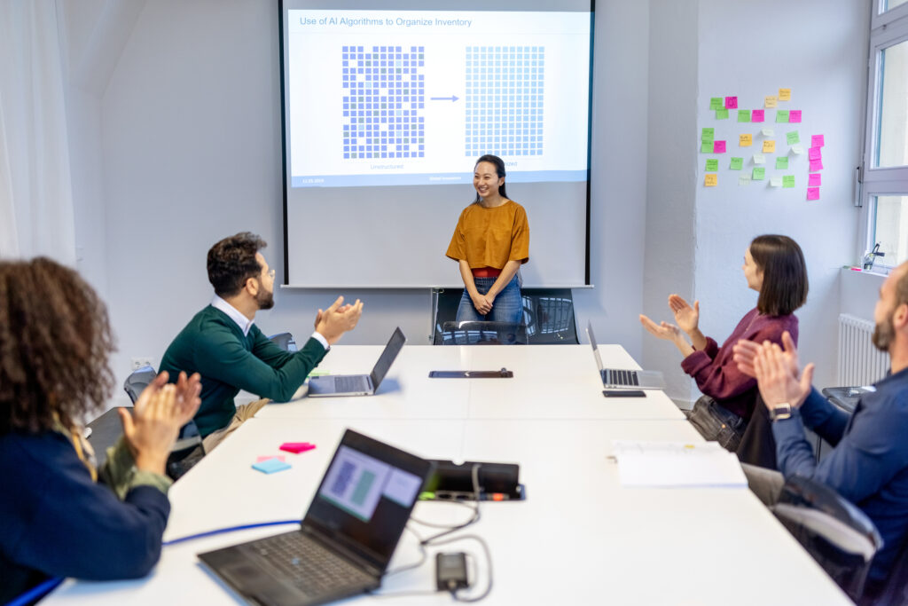 Multi-ethnic business team applauding after a successful artificial intelligence presentation in tech company. Group of business people clapping and smiling while sitting in the meeting room.