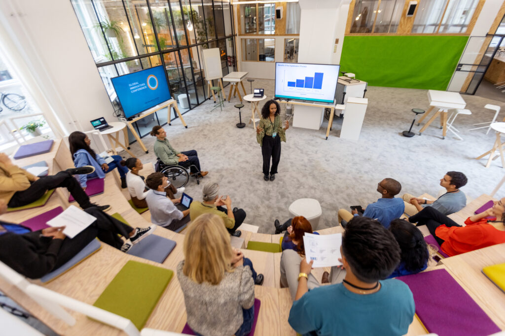 African woman giving speech to group of business people during startup launch event. Multiracial business professionals sitting at seminar hall and listening to young entrepreneur.