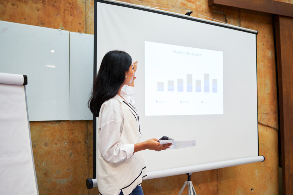 Side view of a Latina businesswoman showing income graphs on a large screen in a modern office at a business seminar.