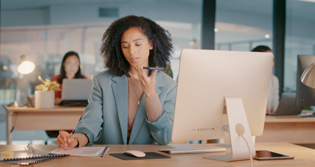 Black woman, office and smartphone call at desk with marketing client for feedback, writing report and notes for advertising agency. African girl, digital marketer working and planning SEO strategy