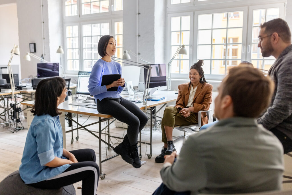 Smiling female manager discussing with professionals during meeting. Entrepreneurs having project meeting at coworking office.