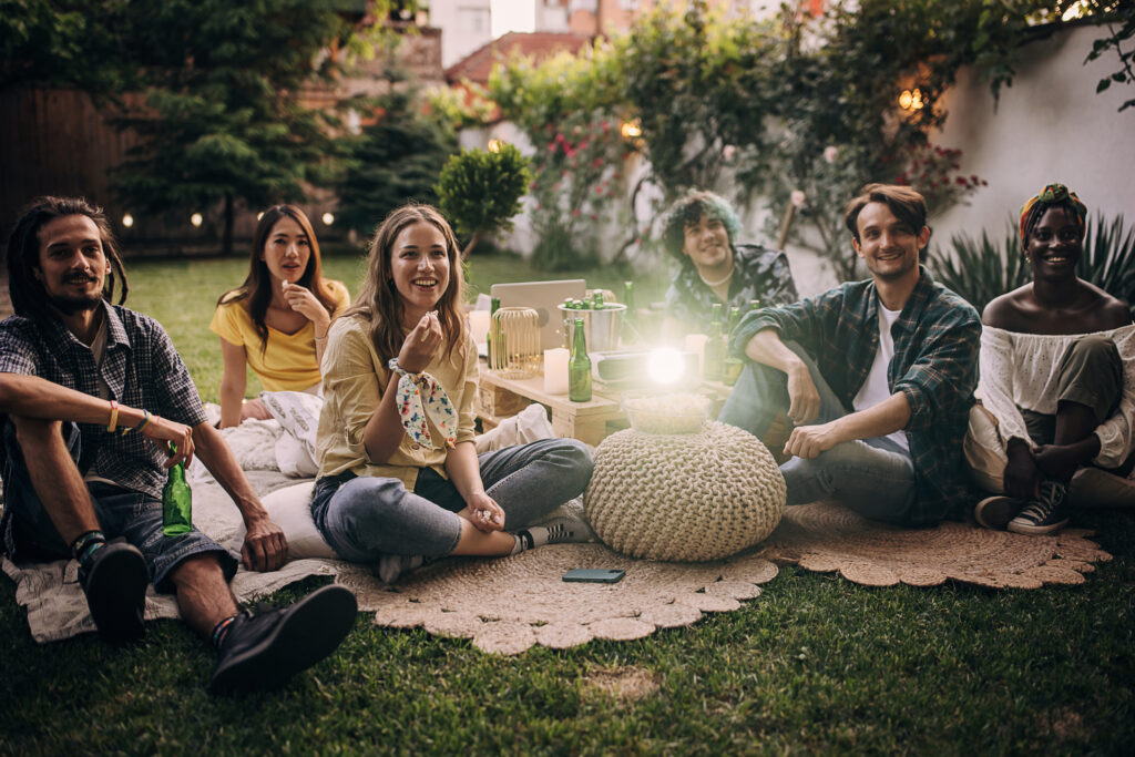 Group of friends having a gathering, watching a movie on projector in the garden and hanging out