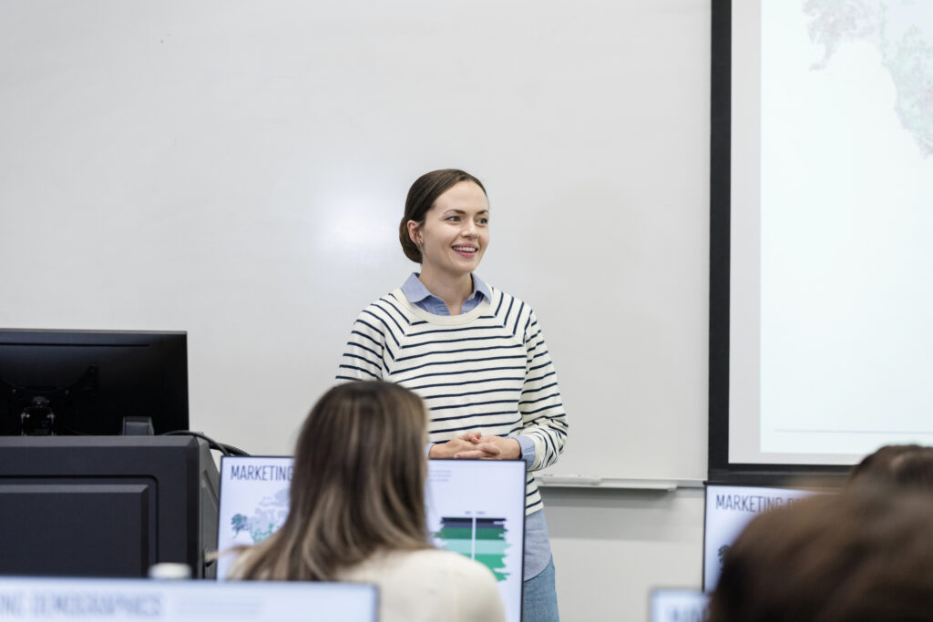 The young adult female university student nervously stands at the front of the class to present her project.