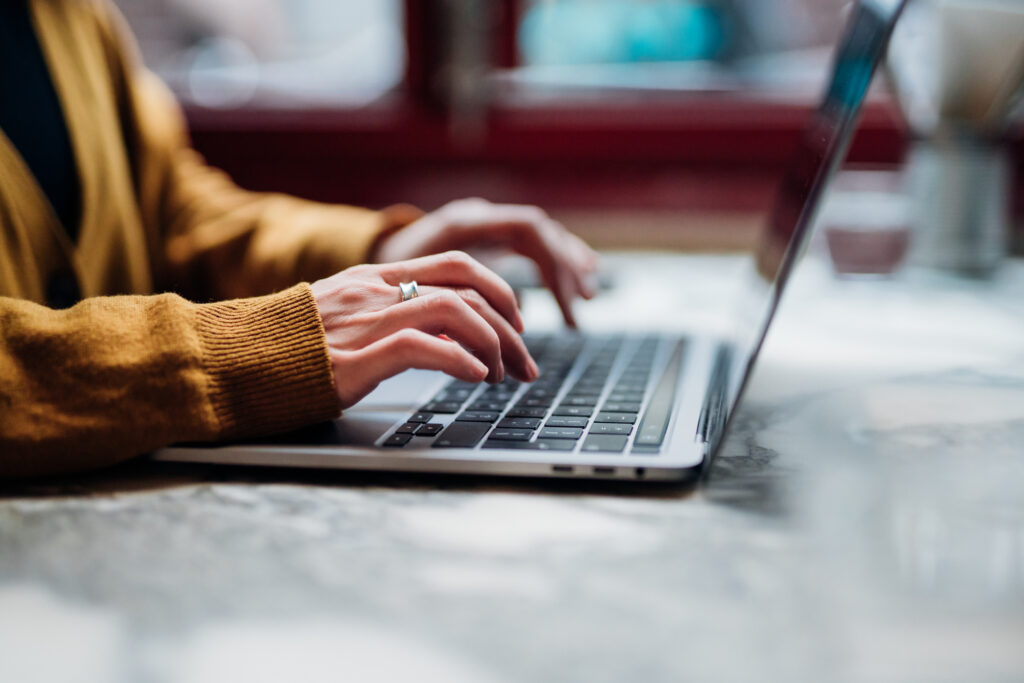 Side view of female hand typing on laptop keyboard. Freelancer working with laptop at cafe. Technology and flexible working.