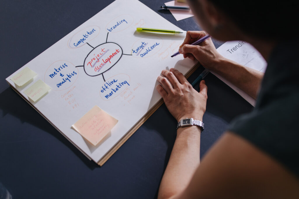 A close up view of an unrecognizable Caucasian entrepreneur holding a marker and planning some business strategy while sitting at her office desk.