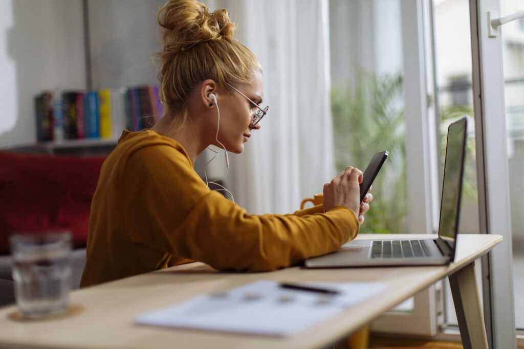 Young blond woman using her cellular phone while working from home