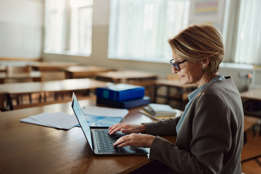 Smiling mature female teacher working on a computer at high school.