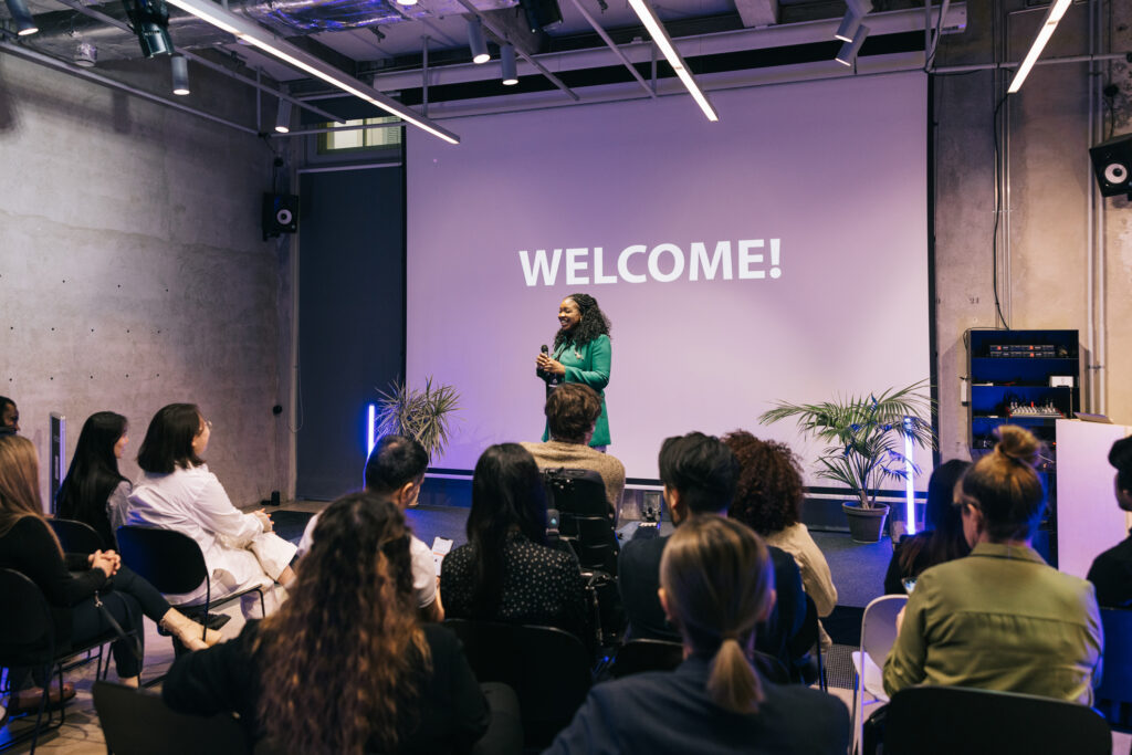 Against the backdrop of a startup tech conference, a business entrepreneur takes the stage, delivering an impactful presentation. Their confident posture and charismatic delivery hold the audience's attention.