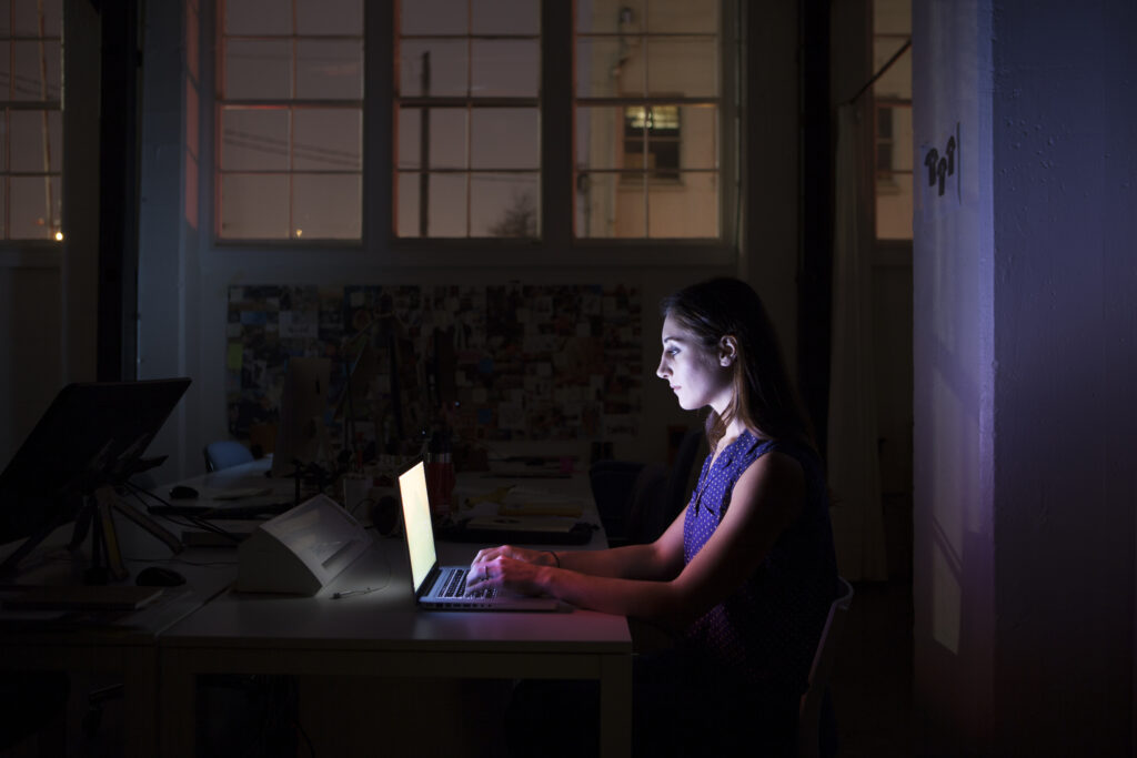 Young employee working late on computer in dark in creative office space.