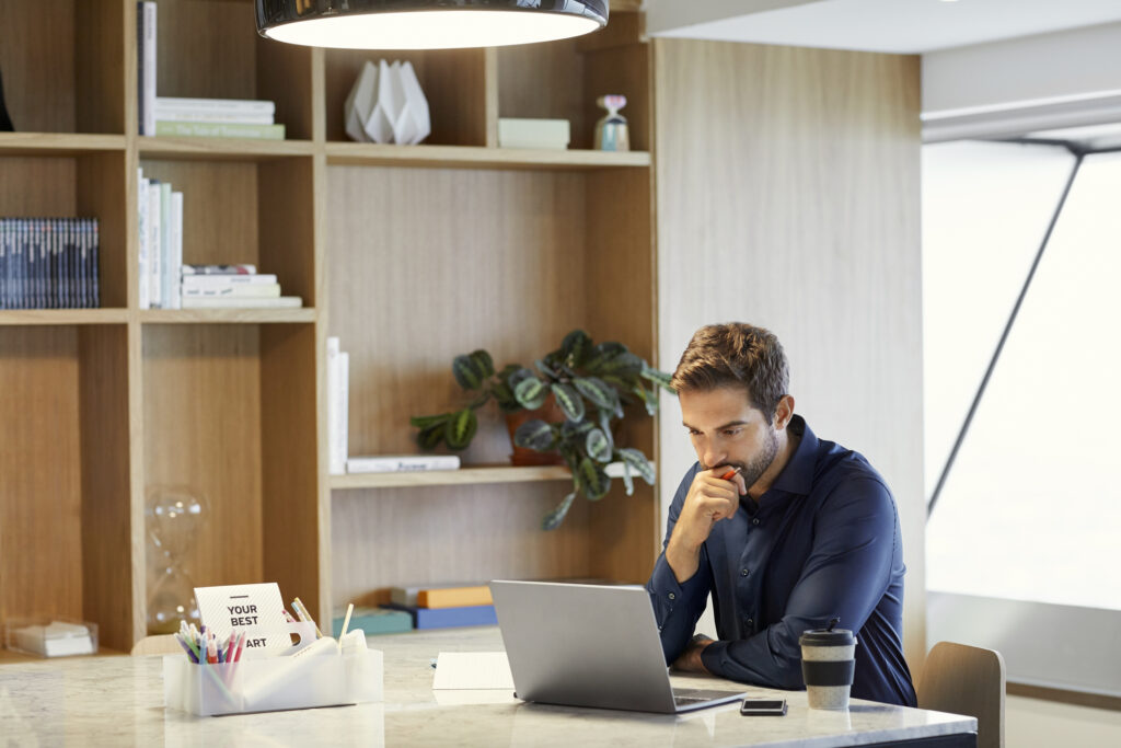 Serious mid adult professional looking at laptop. Confident businessman working at desk. He is concentrating in office.