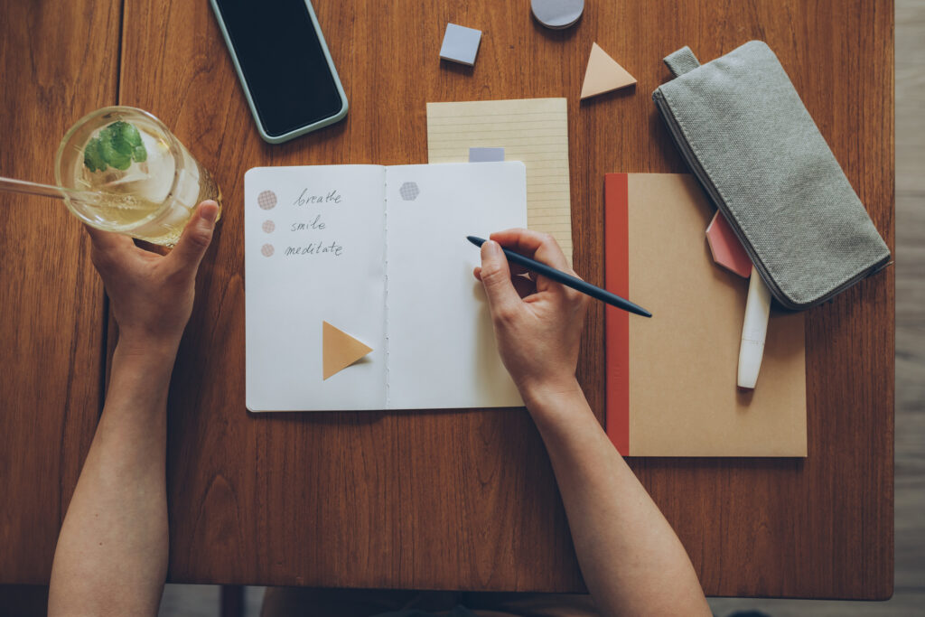 Unrecognizable young woman writing stuff down in a notebook while enjoying a drink in a coffee place