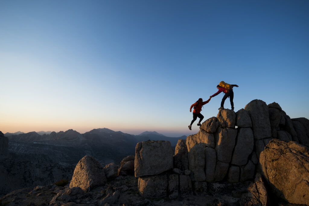 One climber helping the other get to the top of a mountain