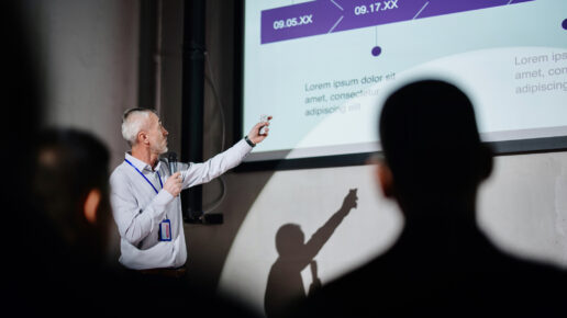 Successful male speaker presents on stage, uses remote control for presentation Showing Infographics