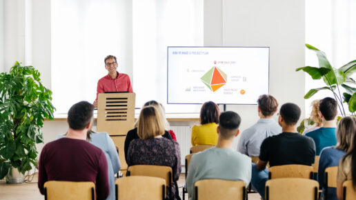 A seminar host standing behind a podium and giving a presentation to a small audience.